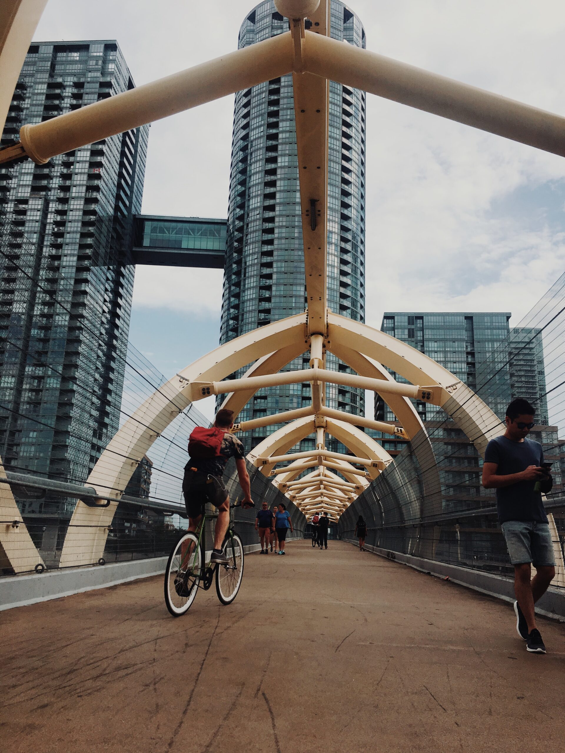 A view looking down the "Puente De Luz" bridge designed by Francisco Gazitua; there is a cyclist on the left and numerous pedestrians; condos in the background