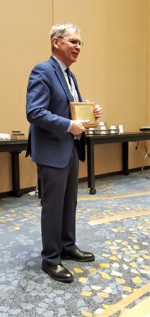 Dr. Brendon Hemily stands with plaque