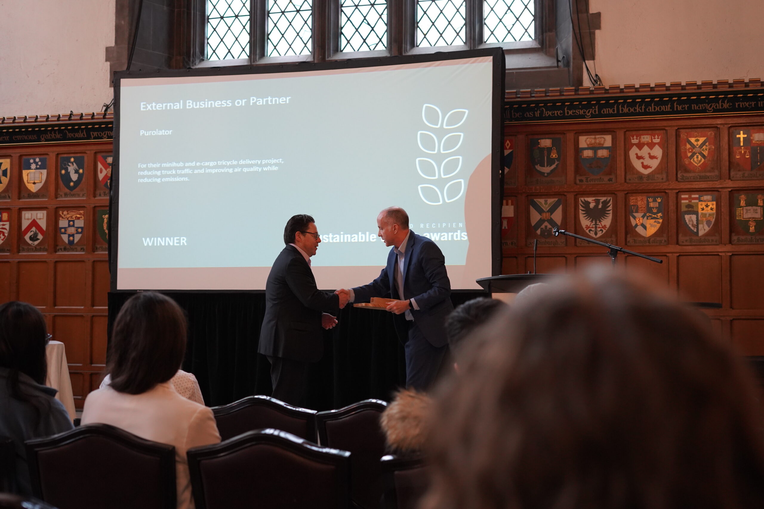 two men shake hands as award is given in front of seated audience.